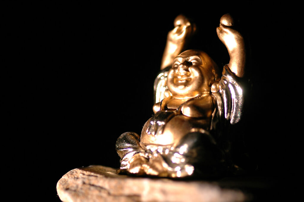 Sinn-Bild #556 Freundlichkeit | lachende Buddah-Figur sitzt auf einem Stein und streckt die Arme in die Höhe. (Bild von Adventuria® – Social Network & Journaling-Plattform für ein persönliches Tagebuch, innerhalb einer Tagebuch-Community mit psychologischer Unterstützung durch Podcasts)