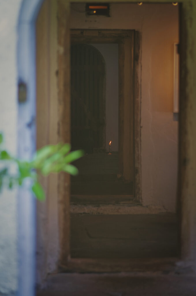 Sinn-Bild #578 Kostbar | Ein Blick durch eine offene Tür, im Haus brennt eine am Boden stehende Kerze. (Bild von Adventuria® – Social Network & Journaling-Plattform, mit einem Tagebuch-Tool, einer unterstützenden Gemeinschaft und psychologischen Ratschlägen durch Podcasts)
